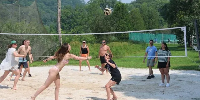 Guests playing beach volleyball on a sand court surrounded by trees