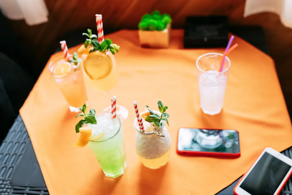 Colorful mocktails with straws and mint on an orange table