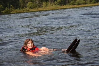 Beginner in a life jacket floating in the lake with skis up, ready to start