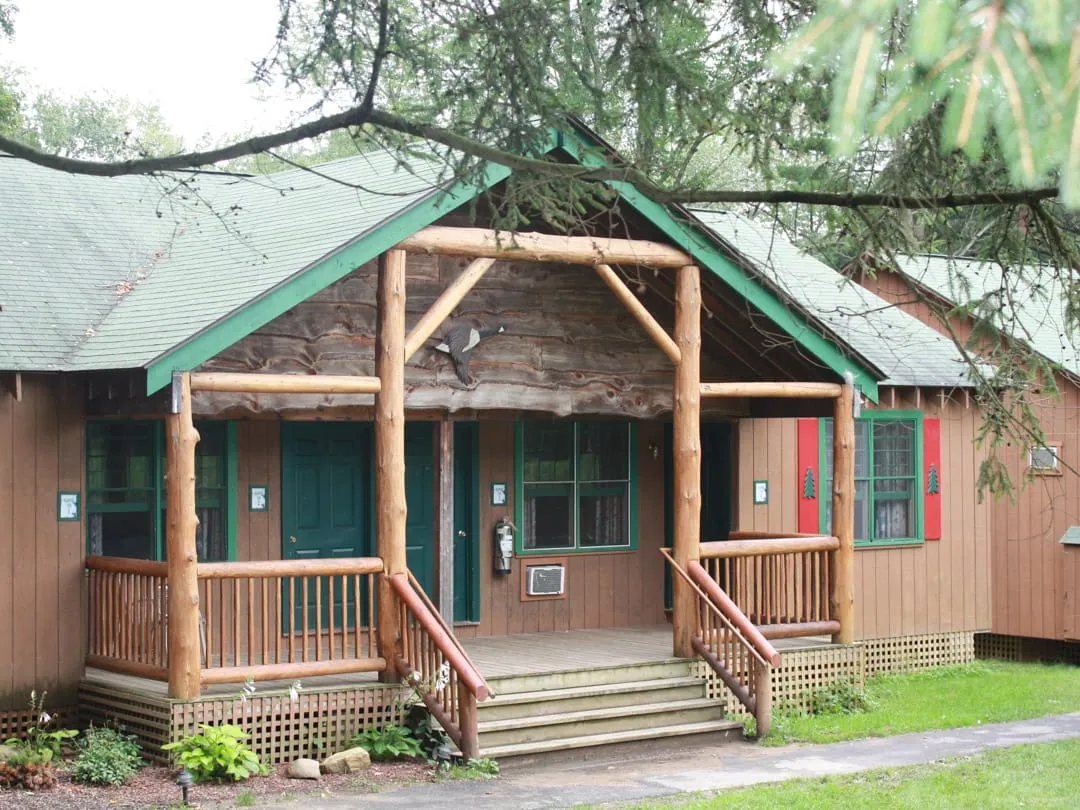 Brown wooden cabin with a log-post porch and green trim on a grassy lawn