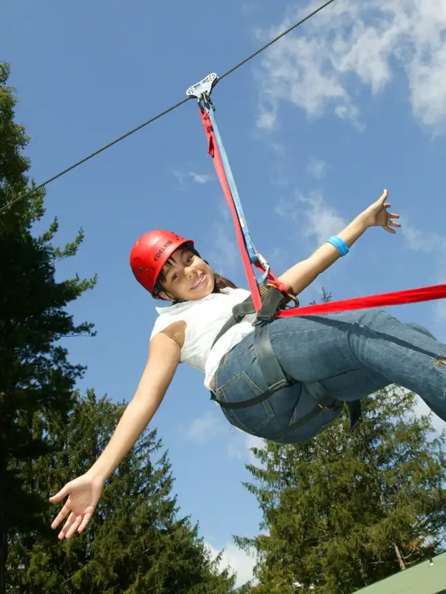 A smiling girl in a red helmet flies down the zip line with her arm outstretched