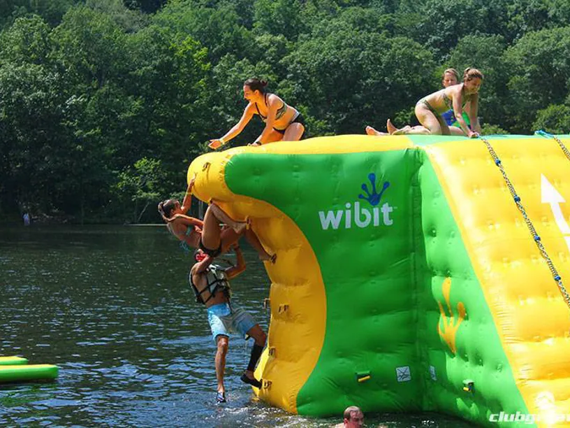 Guests climbing a green and yellow inflatable water iceberg on the lake