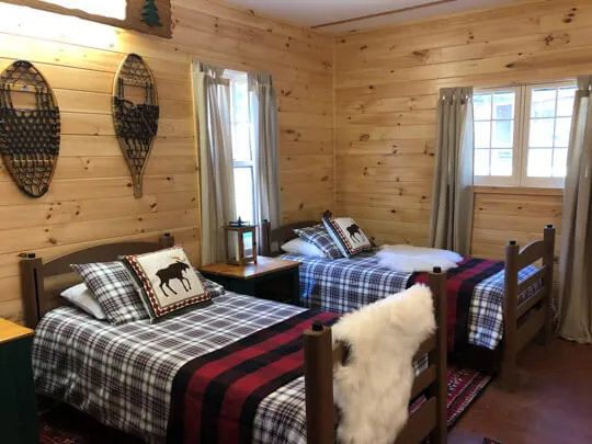 Wood-paneled cabin room with plaid-covered twin beds