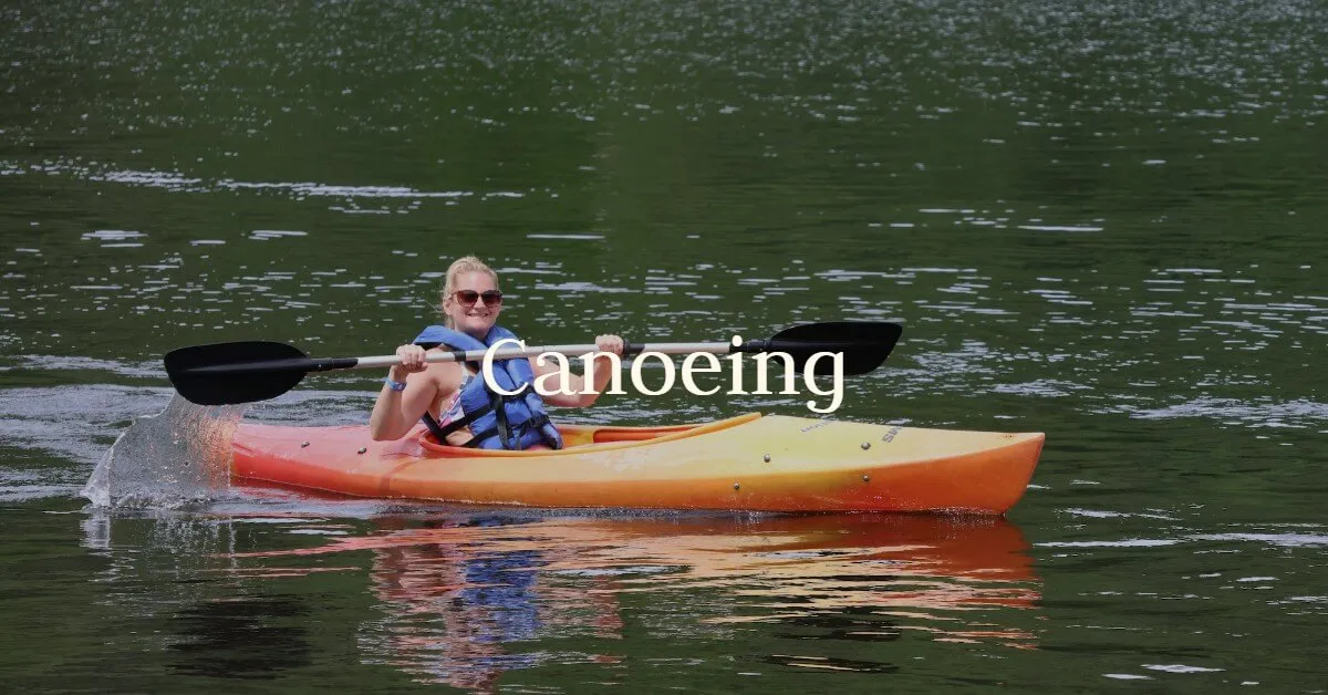 A guest paddles an orange kayak near the shore