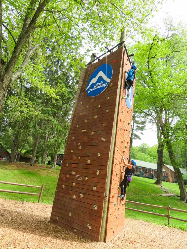 Kids climbing a tall wooden climbing tower among green trees