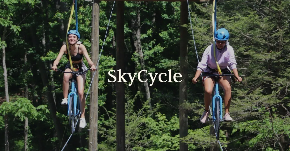 Two guests pedal bicycles along a high wire between the trees