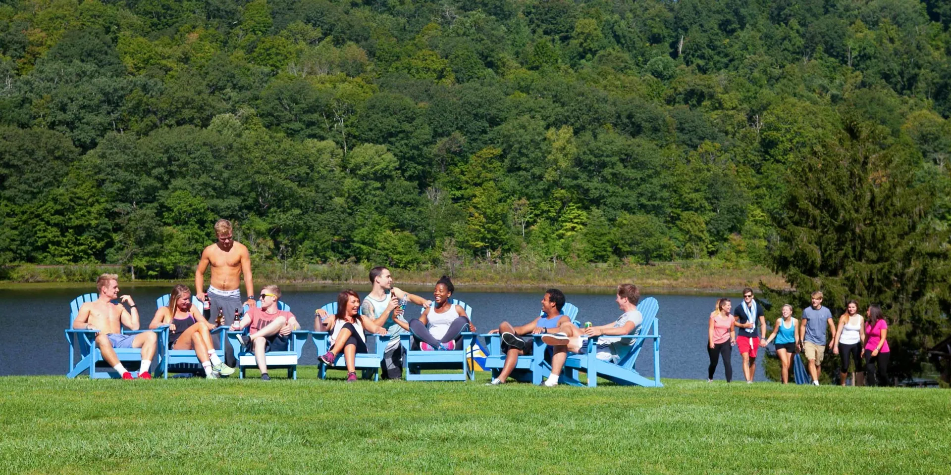 Guests lounging in blue Adirondack chairs on the lawn by the lake