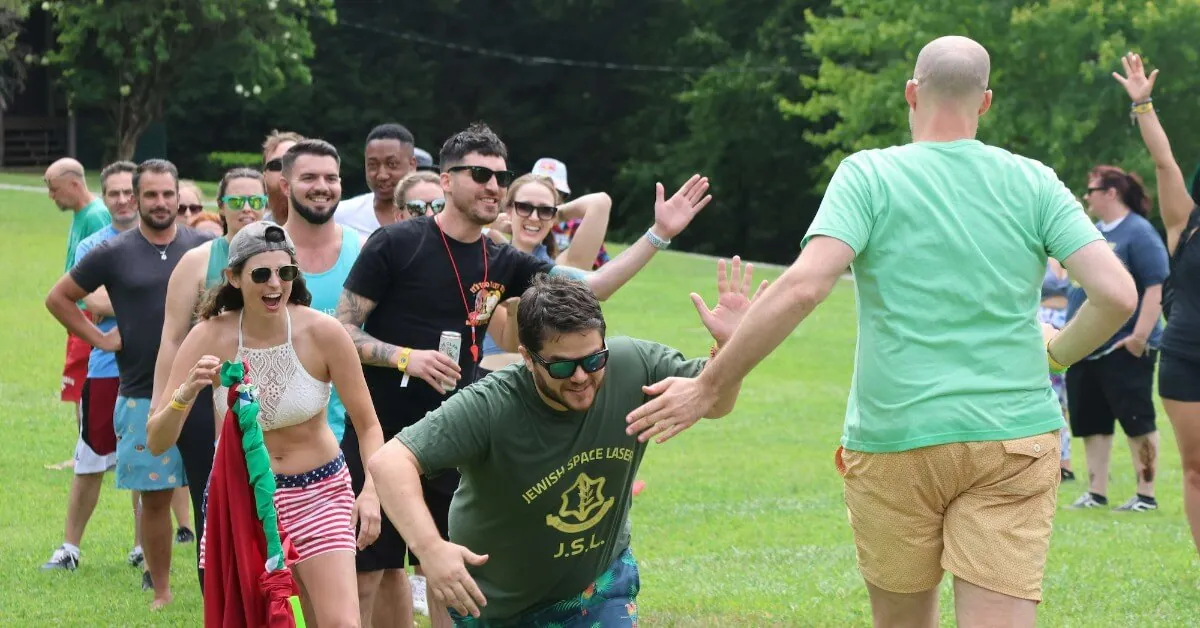 Guests cheer and high-five teammates during a relay race on a grassy field