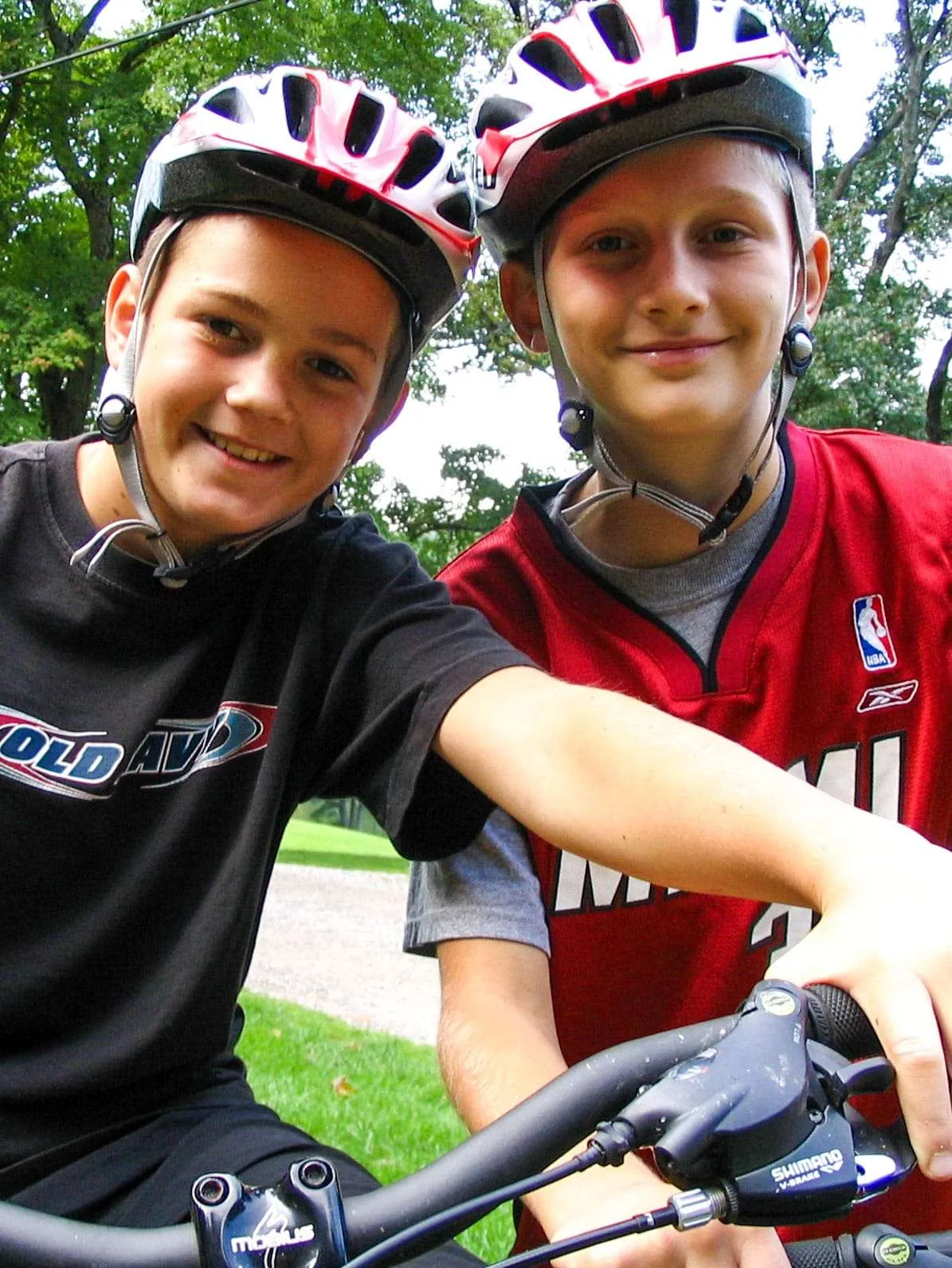 Two grinning boys in bike helmets lean over their handlebars