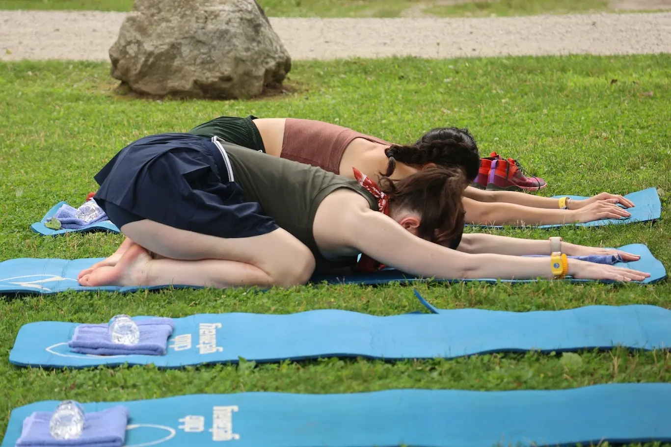 Two women in child's pose on blue yoga mats on the lawn
