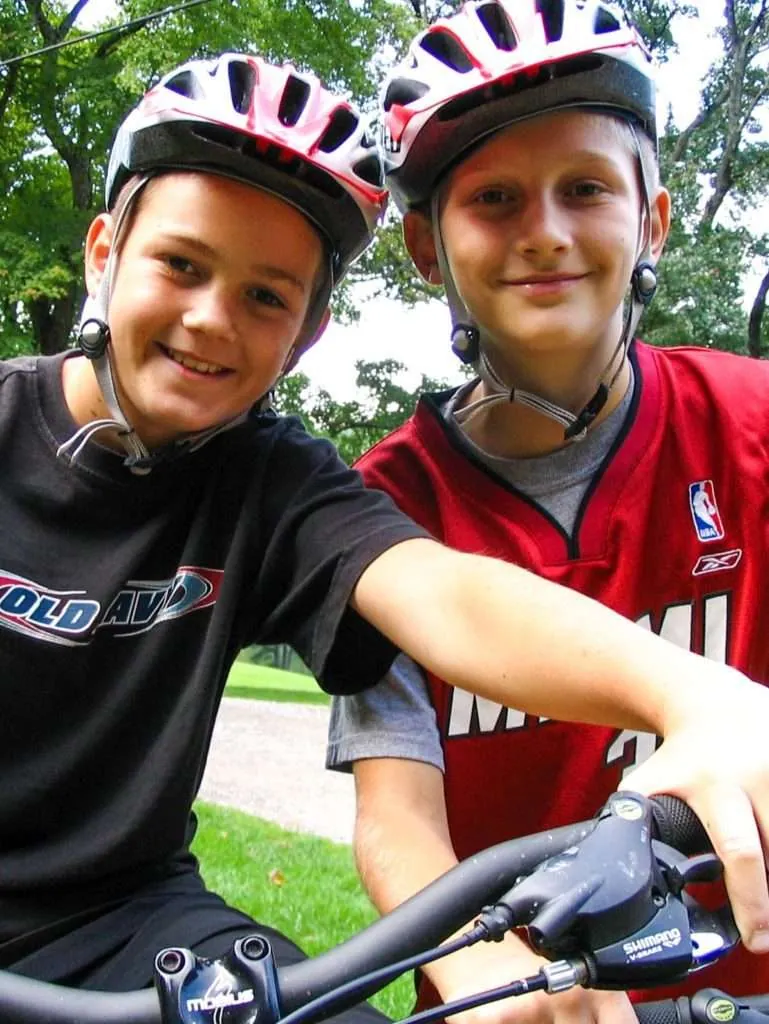 Two grinning boys in bike helmets lean over their handlebars
