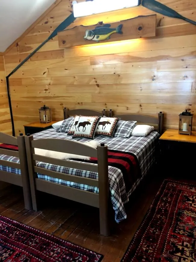 A wood-paneled cabin room with plaid-blanket twin beds and lanterns on the nightstands