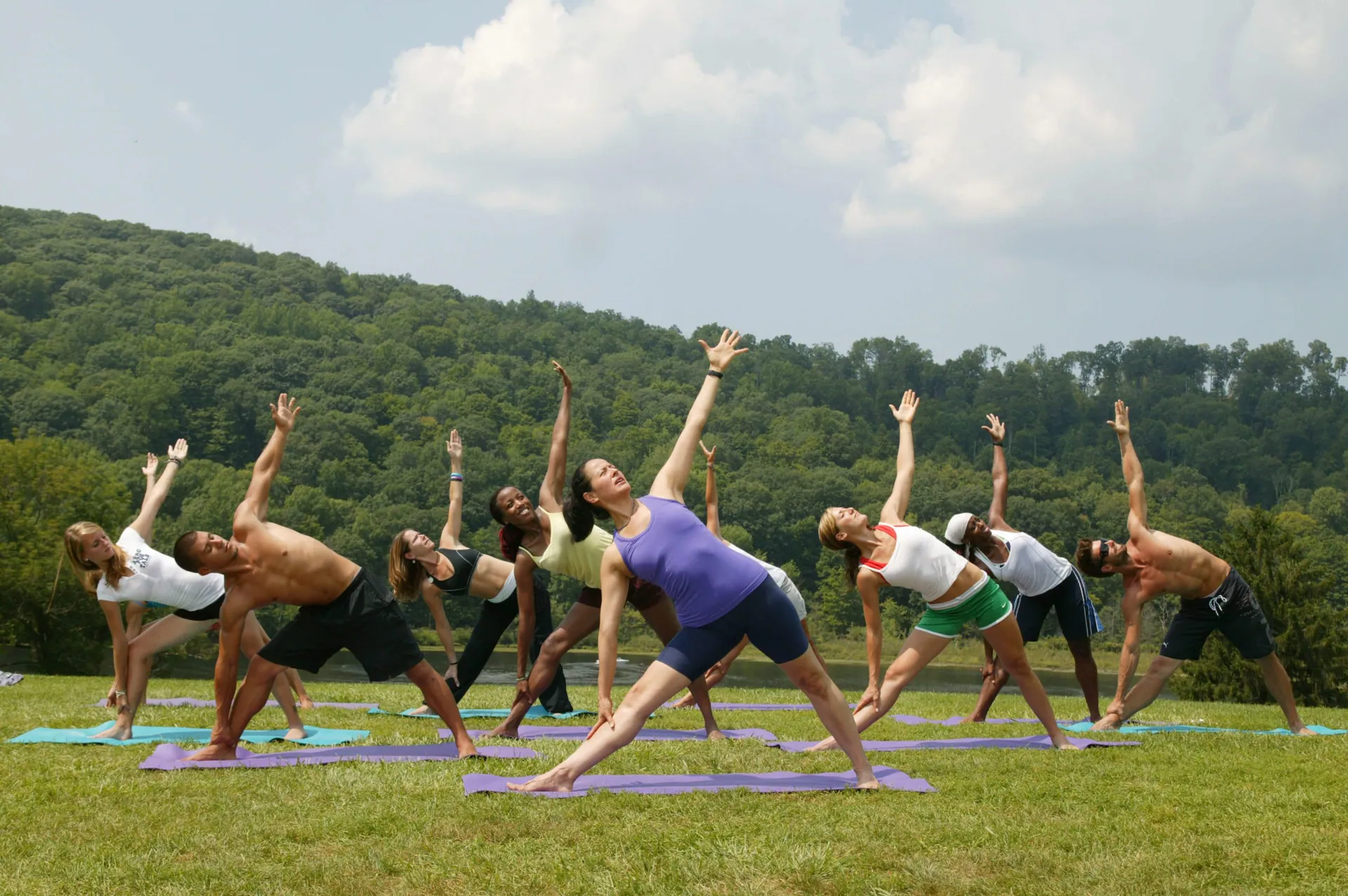 Yoga class in a triangle pose on the lawn with wooded hills behind