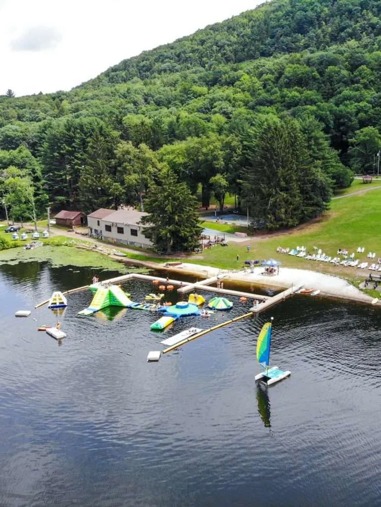 Aerial view of the camp lake with a floating water park and docks below wooded hills