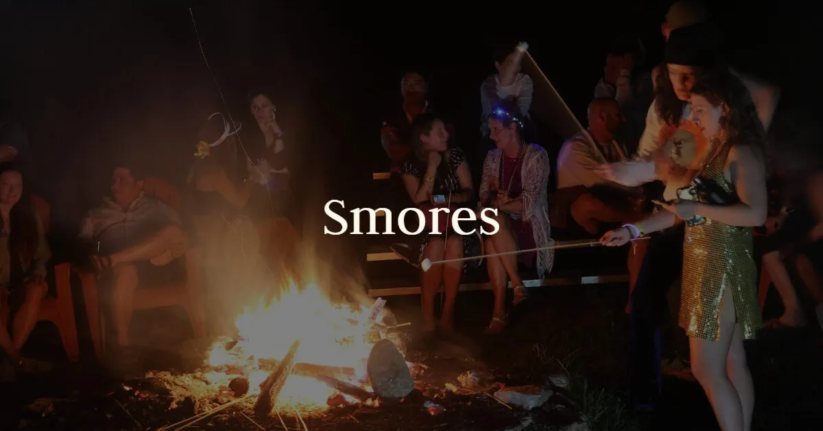 Guests roast s'mores around a crackling campfire at night