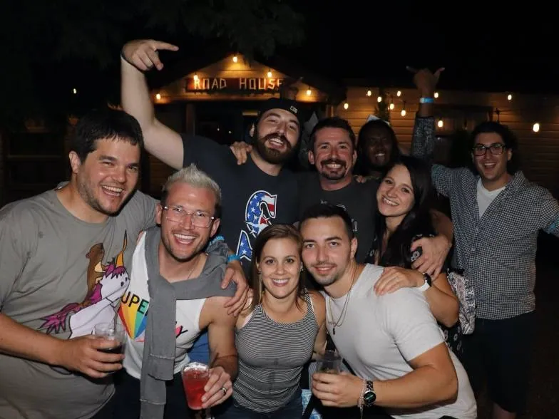 Group of friends smiling and raising drinks outside the Road House at night