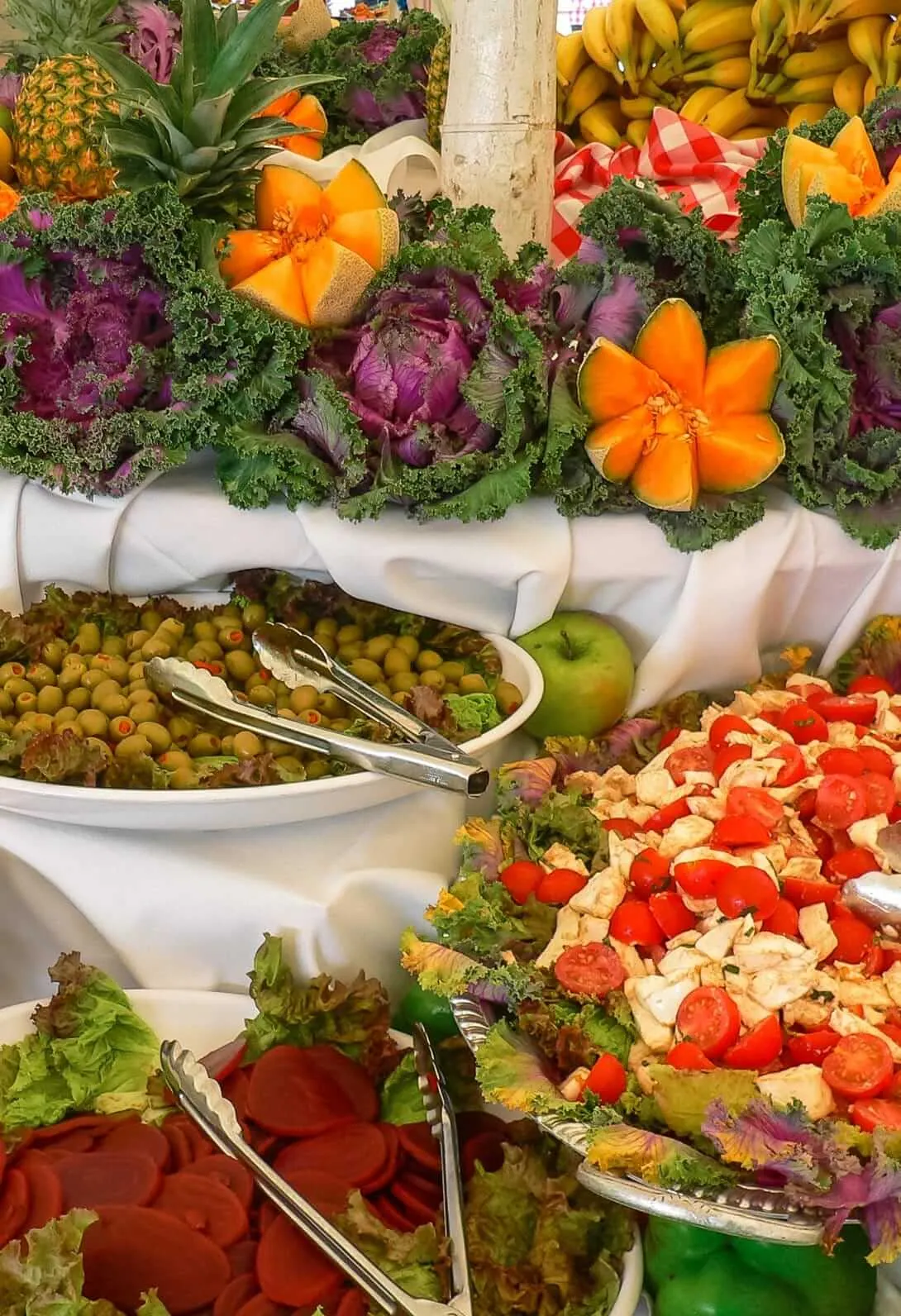 Buffet of fresh fruit, salads and sliced vegetables decorated with kale and carved melon flowers